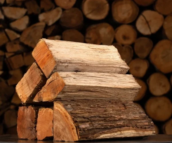 Pile of hickory firewood against a larger stack, showcasing a face cord of wood.