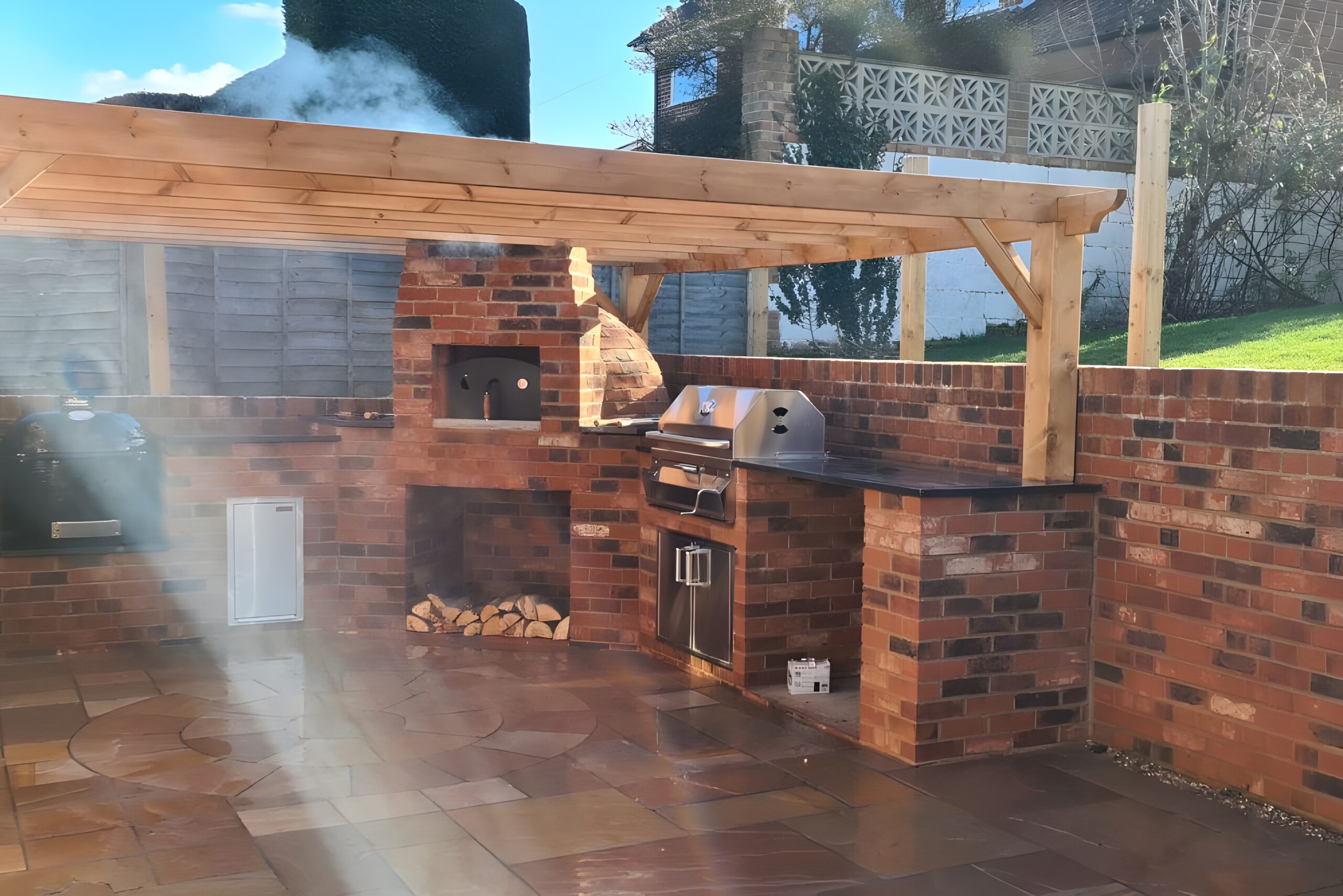 Brick outdoor kitchen with oven, grill, and countertops under a pergola.