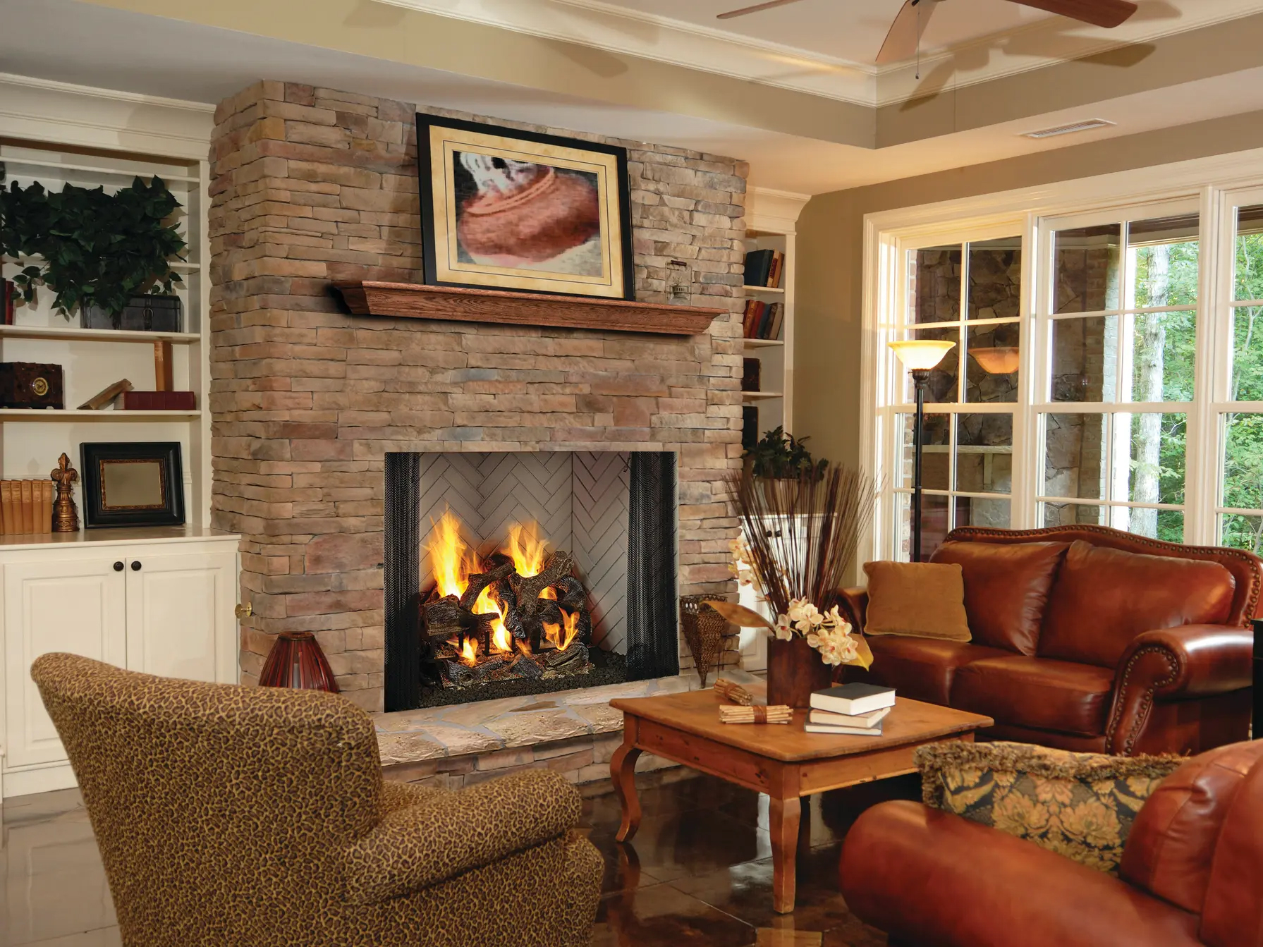 A cozy living room with a stone fireplace, leather furniture, and large windows letting in natural light.