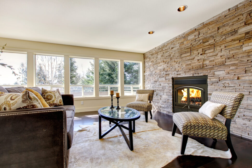 Cozy living room with a stone fireplace, patterned chairs, and large windows.