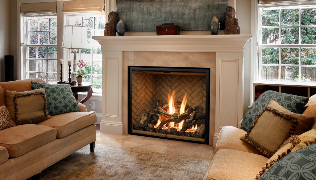 A cozy living room featuring a traditional fireplace, beige sofas with decorative pillows, and large windows allowing natural light.